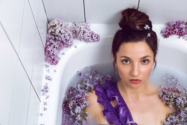 donna in costume da bagno facendo il bagno con latte e fiori lilla