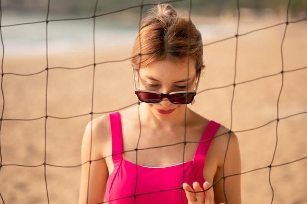 Donna in costume da bagno rosa in posa vicino alle vacanze estive nette di beach volley