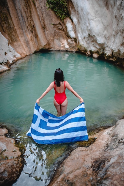 Donna in costume da bagno rosso con bandiera greca Cascata Dimosari al famoso punto di riferimento dell'isola di Lefkada