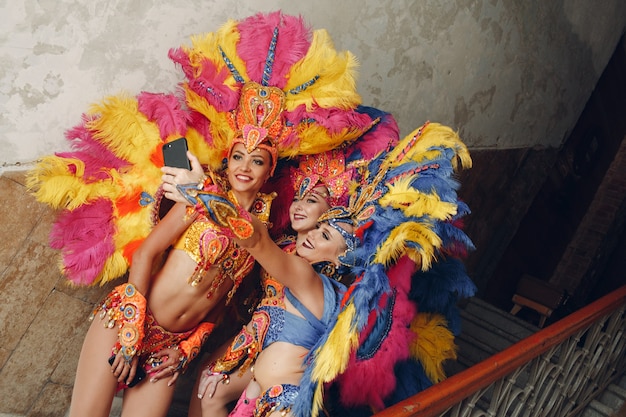 Donna in costume di carnevale samba brasiliano con piume colorate piumaggio con telefono cellulare prendere selfie nel vecchio ingresso con grande finestra.