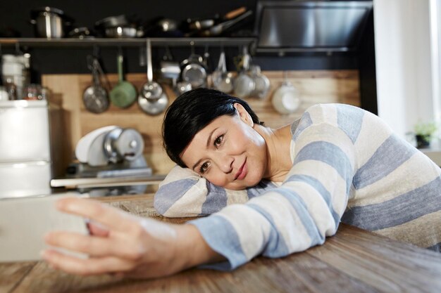 Donna in cucina appoggiata sul tavolo che tiene il cellulare