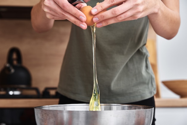 Donna in cucina che cucina un impasto. Le mani rompe un uovo in una ciotola