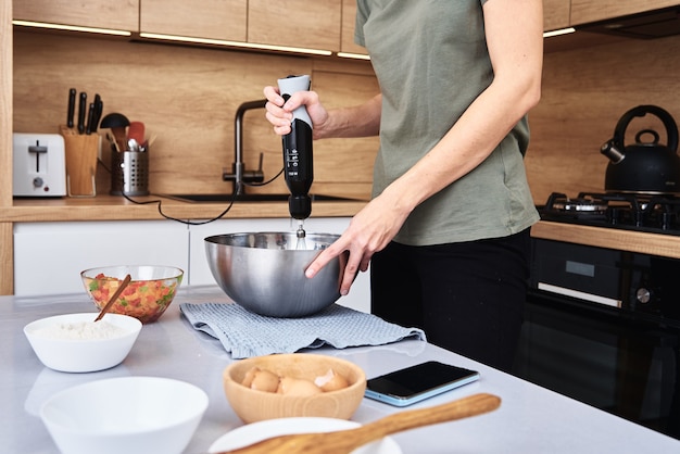 Donna in cucina che cucina una torta. Le mani sbattono l'impasto con una frusta elettrica