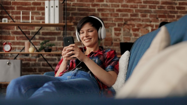 Donna in cuffia ascoltando musica su smart phone utilizzando l'app musicale. Relax, svago.