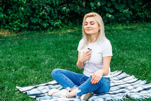 Donna in cuffia e con uno smartphone in mano seduto sull'erba all'aperto nel parco