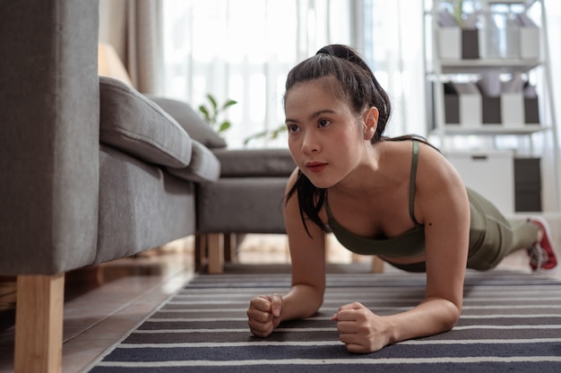 Donna in forma che fa la tavola da yoga e guarda tutorial online sull'allenamento del laptop in soggiorno