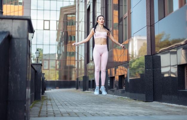 Donna in forma che si esercita a saltare la corda sullo sfondo di un edificio cittadino Stile di vita sano allenamento cardio