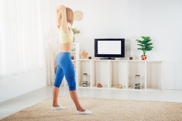 Donna in forma che si riscalda mentre fa esercizi di stretching a casa davanti alla TV.