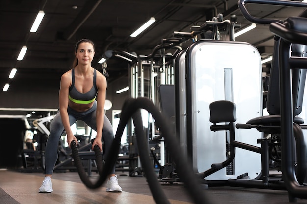 Donna in forma che utilizza corde da battaglia durante l'allenamento della forza in palestra.