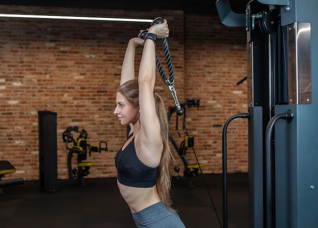 Donna in forma con tricipiti perfetti per l'allenamento del corpo con macchina per esercizi via cavo in palestra