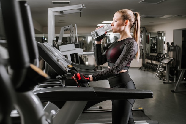 Donna in forma sul tapis roulant con bottiglia d'acqua in palestra