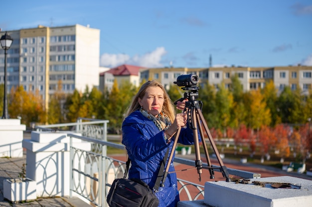 donna in giacca blu con treppiede e videocamera riprende un paesaggio autunnale