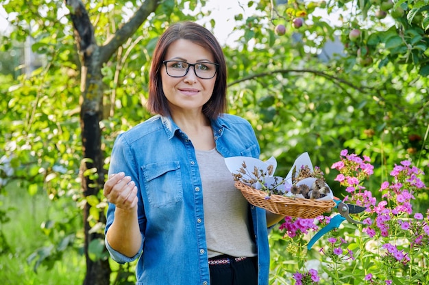 Donna in giardino estivo con semi di piante di fiori secchi raccolti in cestino