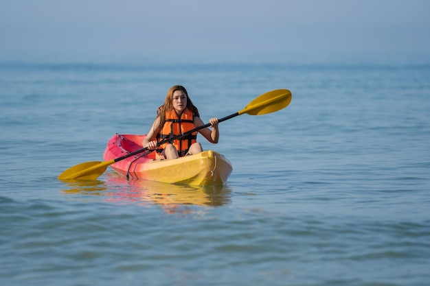 Donna in giubbotto di salvataggio che rema un kayak in mare
