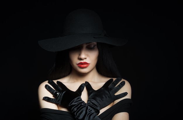 Donna in grande cappello nero con le braccia su sfondo scuro ritratto in studio