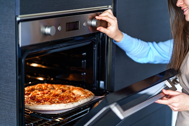 Donna in grembiule che cucina pizza casalinga per la cena facendo uso del forno