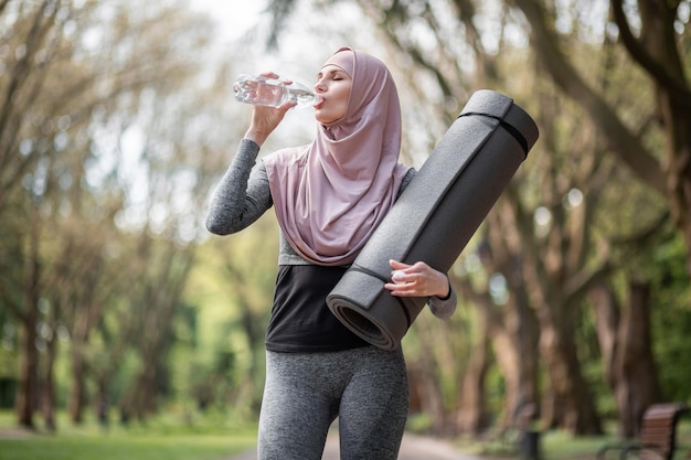 Donna in hijab e acqua potabile activewear al parco