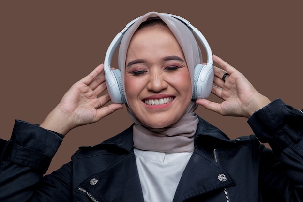 Donna in hijab in posa indossando cuffie wireless con sorridente mentre chiude gli occhi