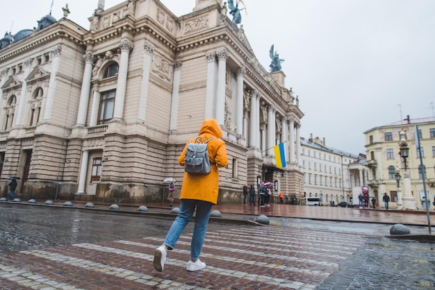 Donna in impermeabile arancione che attraversa il vecchio edificio europeo sullo sfondo della strada