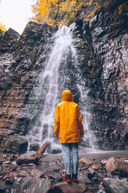 Donna in impermeabile giallo al concetto di escursione della cascata d'autunno