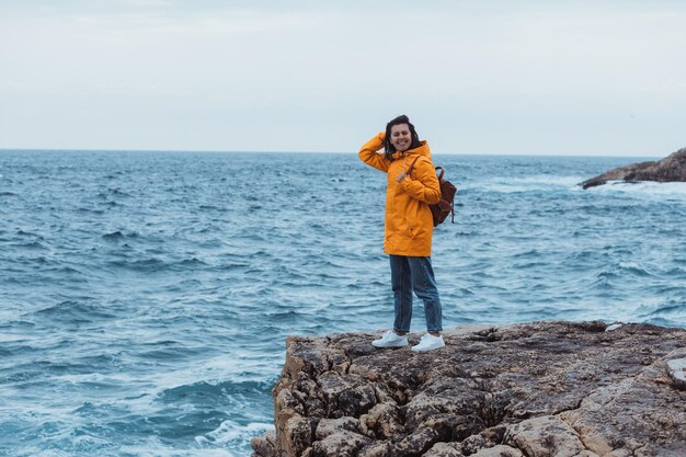 Donna in impermeabile giallo sulla scogliera che gode della vista sul mare durante le tempeste