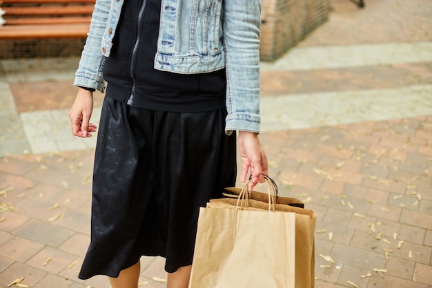 Donna in incognito che tiene diversi sacchetti di carta con cose acquistate che camminano all'aperto nel parco, ragazza dopo lo shopping.