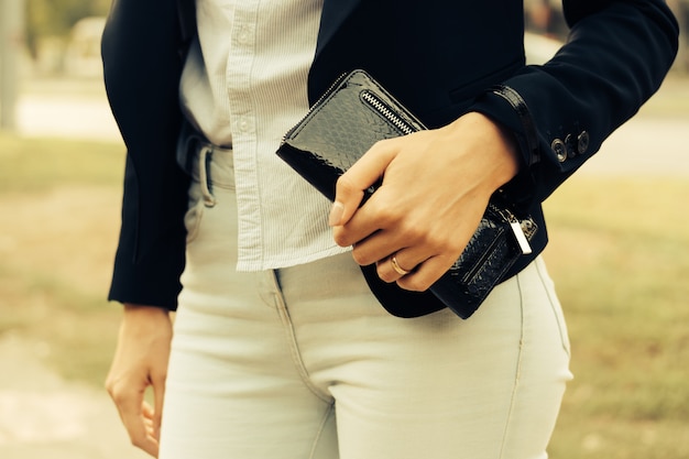 Donna in jeans, camicia e una giacca nera che tiene una borsa in mano all&#39;aperto