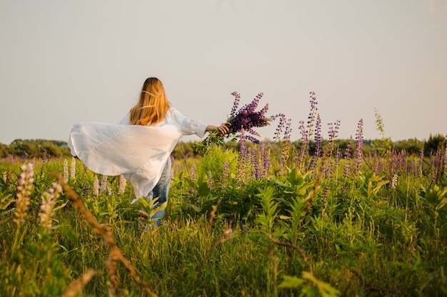 Donna in jeans e mantello bianco che attraversa il campo