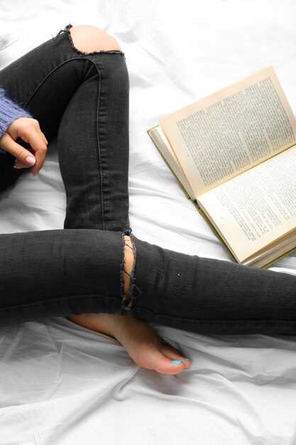 Donna in jeans neri che legge libro sul punto di vista superiore del letto