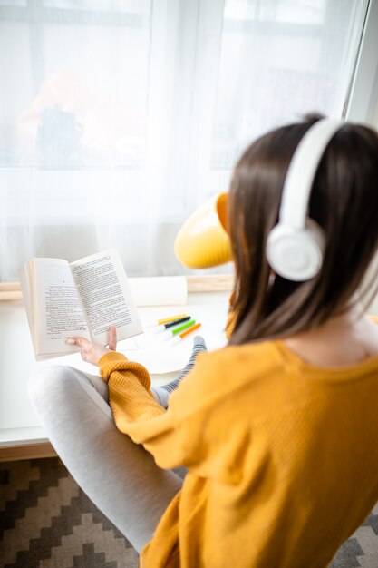 Donna in libro di lettura delle cuffie a casa, svago di quarantena.