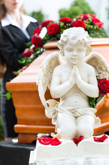 Donna in lutto al funerale con una rosa rossa in piedi alla bara o alla bara