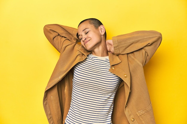 Donna in maglietta a righe e camicia denim sullo sfondo giallo che si sente sicura con le mani dietro la testa