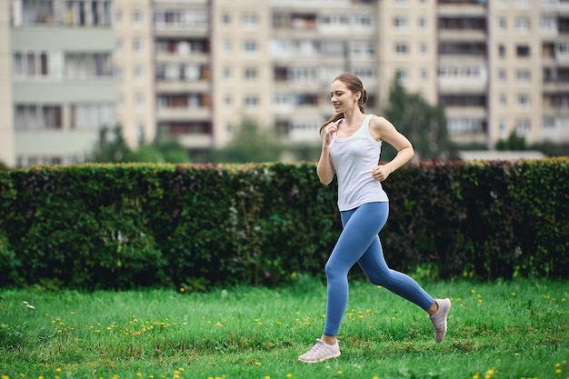 Donna in maglietta bianca e leggings fa jogging mattutino nella zona residenziale della città vicino al grattacielo