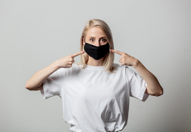 Donna in maglietta bianca e maschera facciale nera sul muro bianco