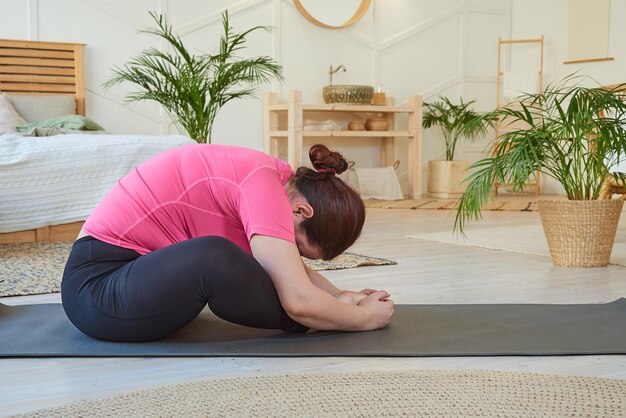 Donna in maglietta rosa che fa stretching sul tappetino da yoga sul pavimento di casa