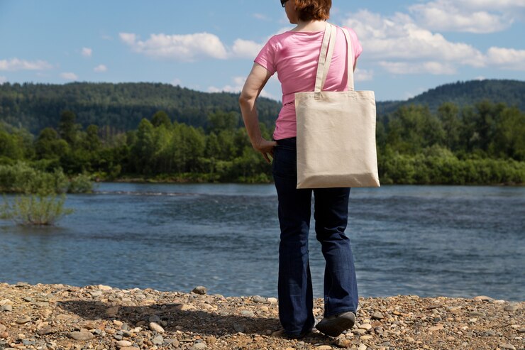 Donna in maglietta rosa che trasporta mockup di borsa della spesa riutilizzabile vuota.