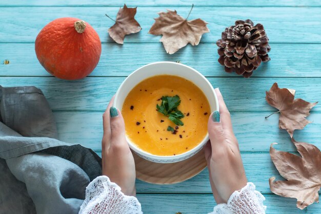 Donna in maglione che tiene ciotola con zuppa di crema di gamberi e zucca, concetto di cibo autunnale, vista dall'alto