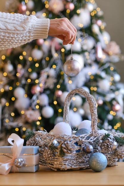 Donna in maglione di lana caldo bianco che tiene la palla decorativa del giocattolo in mani sui precedenti di un albero di Natale. Natale, concetto di celebrazione delle vacanze di capodanno. Messa a fuoco selettiva