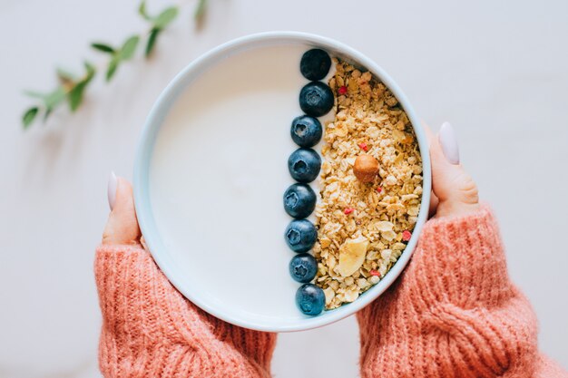 Donna in maglione di lana corallo che mangia la prima colazione con muesli e yogurt, bacche e nocciole