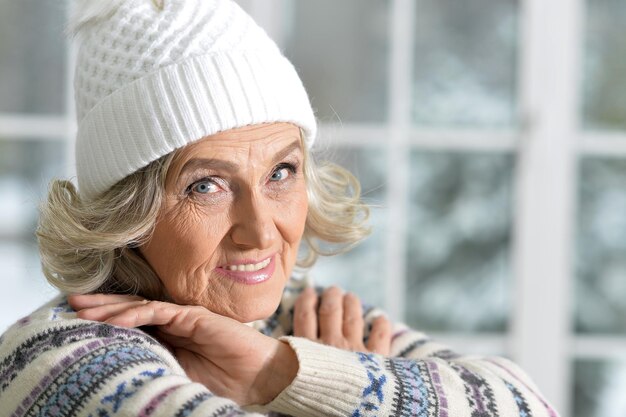 Donna in maglione e cappello bianco in posa vicino alla finestra, primo piano