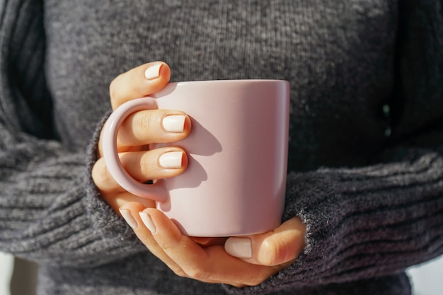 donna in maglione lavorato a maglia grigio che tiene una tazza con bevanda calda