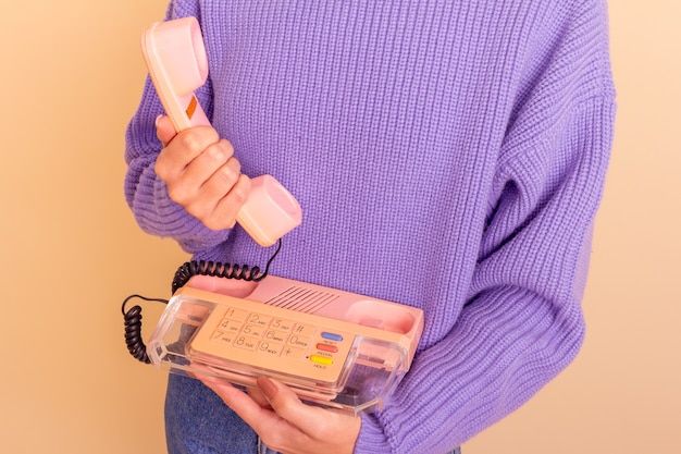 Donna in maglione lilla, jeans e calzini in possesso di un telefono. Sfondo beige.