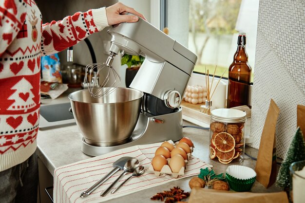 Donna in maglione natalizio festivo che prepara la pasta per i biscotti a casa cucina mani femminili usano elec