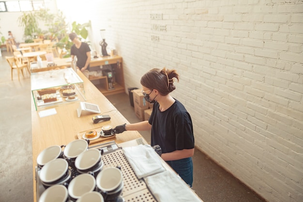 Donna in maschera che lavora barista in una caffetteria