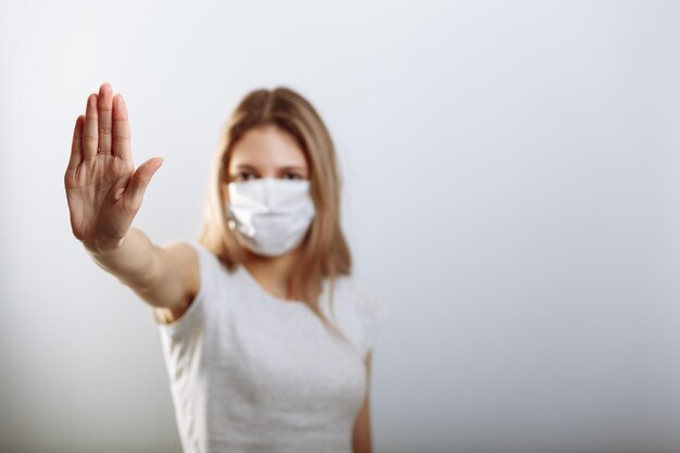 Donna in maschera facciale che mostra il segnale di stop con la mano per prevenire la diffusione dei virus Messa a fuoco selettiva