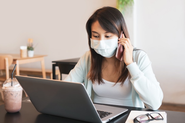 donna in maschera medica che lavora mentre parla al telefono. affari e tecnologia, concetto di assistenza sanitaria.