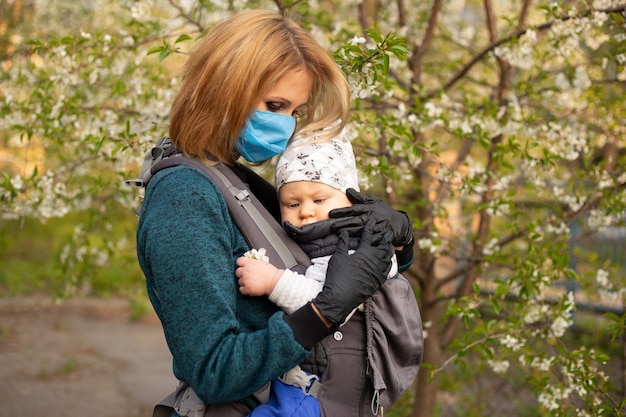 Donna in maschera medica con un bambino in braccio Gioia della maternità e dello sviluppo del bambino albero in fiore in tarda primavera