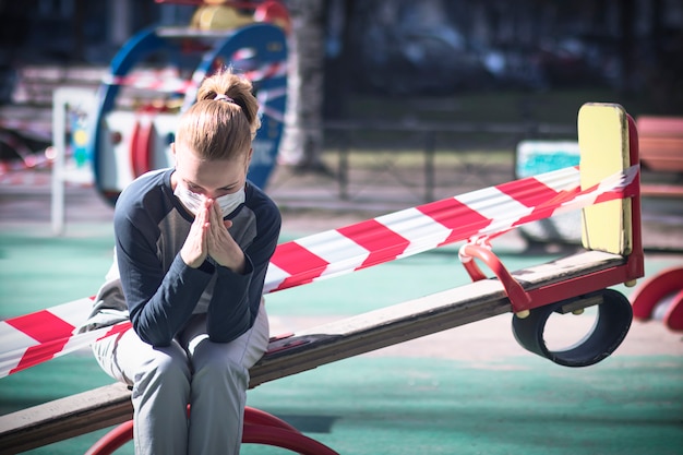 donna in maschera medica si siede su un parco giochi