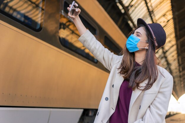 Donna in maschera prendendo selfie alla stazione ferroviaria