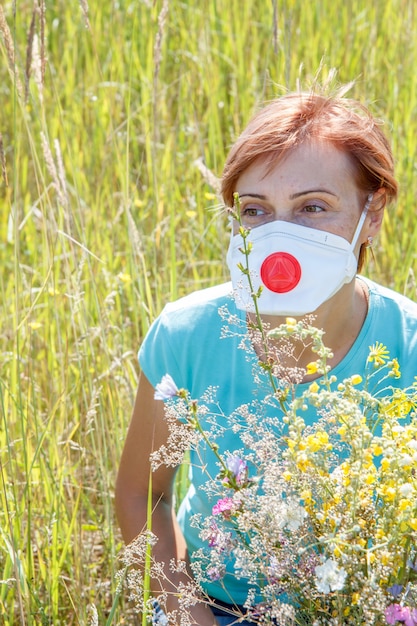 Donna in maschera protettiva che tiene un mazzo di fiori di campo e cerca di combattere le allergie al polline.